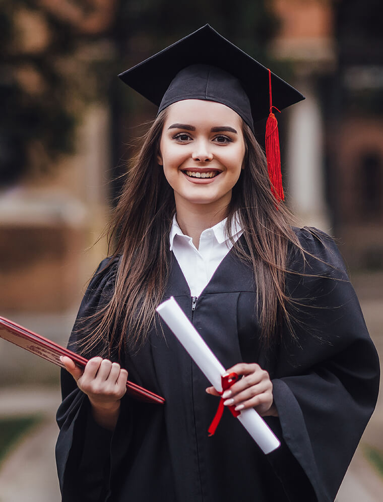 Student in graduation regalia in front of the UT tower, showing hook 'em hand signal